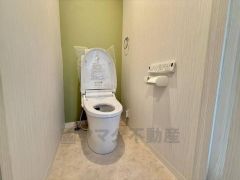温水洗浄便座を標準装備した、清潔感のあるトイレ空間です。上部にはトイレットペーパーのストックを置ける便利な棚が設けられています。
