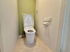 温水洗浄便座を標準装備した、清潔感のあるトイレ空間です。上部にはトイレットペーパーのストックを置ける便利な棚が設けられています。
